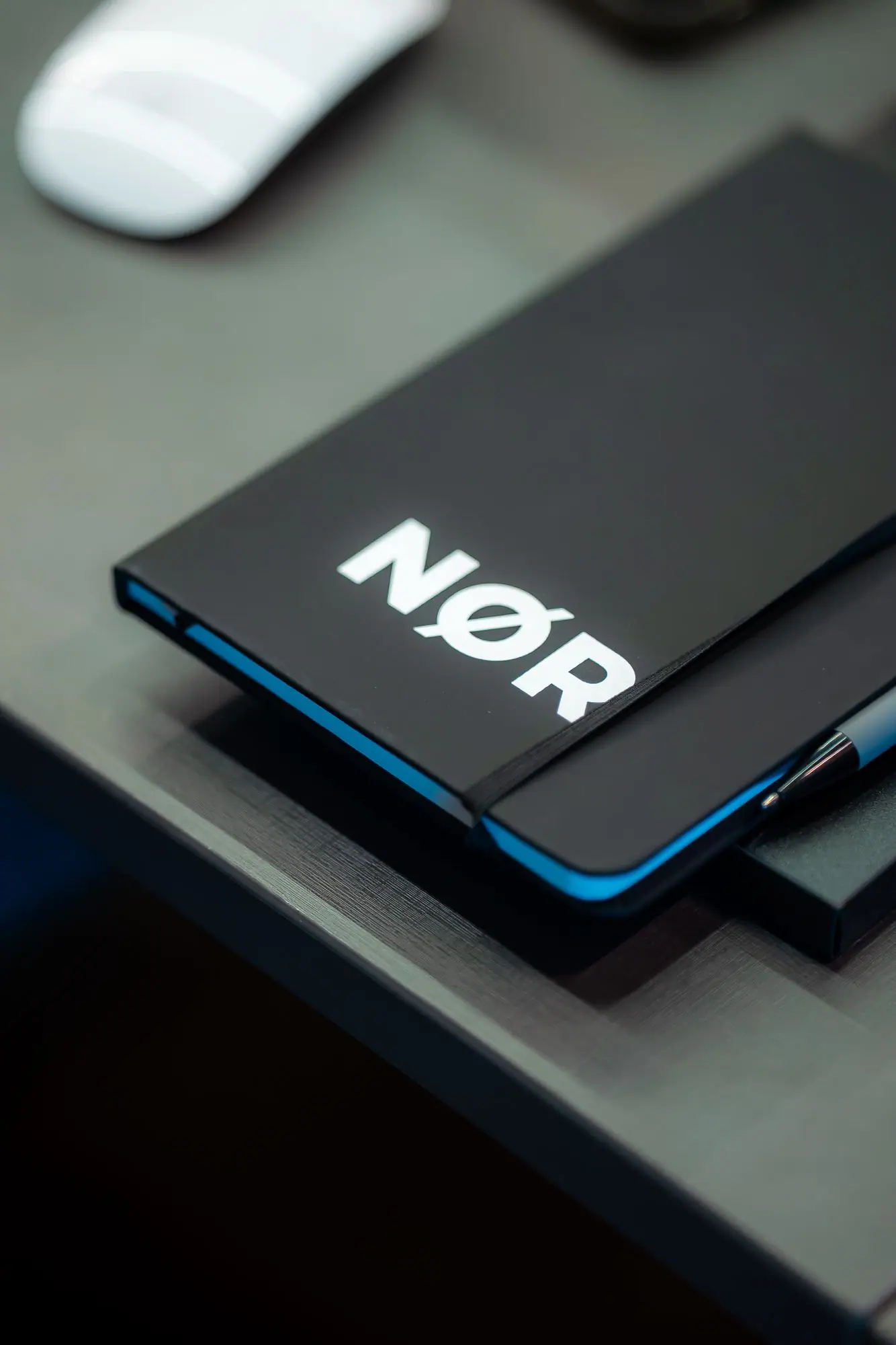 Detalhe de um caderno preto com a marca NØR sobre a mesa.